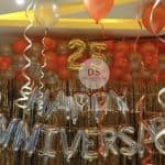 25th Anniversary Decoration Package featuring 90 gold, orange, and silver balloons with a golden backdrop and Happy Anniversary lettering by Dream Spark Events