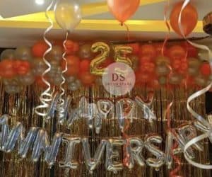25th Anniversary Decoration Package featuring 90 gold, orange, and silver balloons with a golden backdrop and Happy Anniversary lettering by Dream Spark Events
